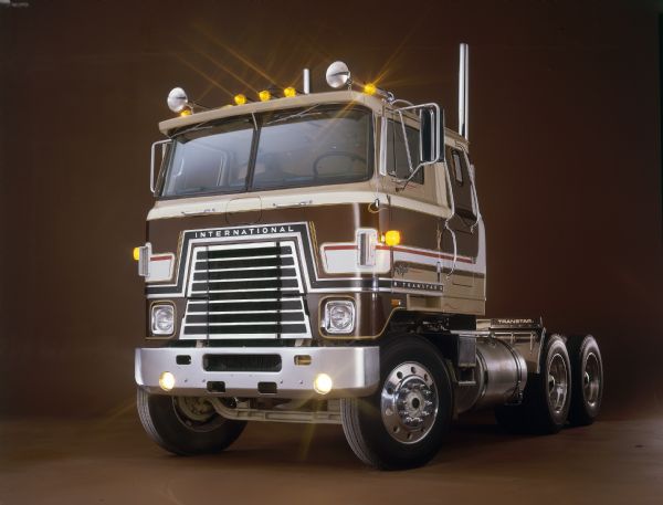Color studio three-quarter view from front of the driver's side of an International Transtar Eagle semi tractor. The truck features a brown and tan color scheme with extensive pinstriping.