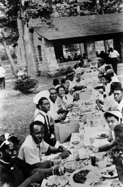 A group of African Americans gathered at a picnic table for an outdoor church picnic.