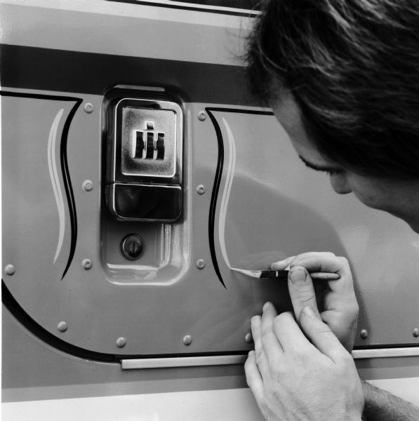 A man adds pinstripes around the door handle of an International Transtar Eagle semi tractor. The IH logo is on the door handle.