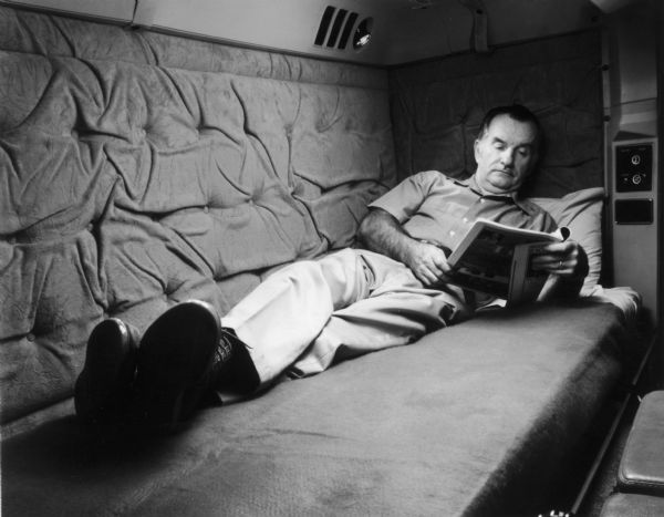 A man reads a magazine while reclining in the sleeper cab of an International Transtar Eagle semi tractor.