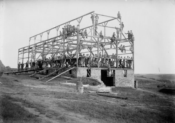 Workers pose on the frame of a barn they are building.