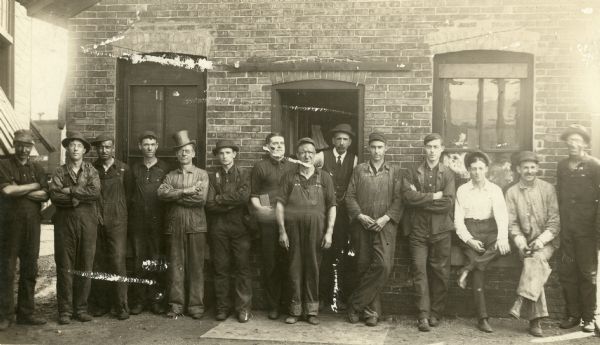 A group of railway shopmen of the Chicago, Milwaukee, and St. Paul Railroad pose at the terminal roundhouse in Madison's west side yards bordering Regent Street. The roundhouse foreman, A.J. (Arthur Jacob) Edmonds, stands in the doorway wearing a vest, tie and hat.