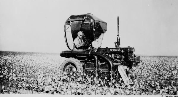 Field test of an experimental International Harvester cotton picker mounted on a Farmall B tractor. The caption reads "Experimental IH low-drum 1-row Farmall mounted cotton picker with clearing and overhead and side-mounted self-unloading hopper attachments - 1944."