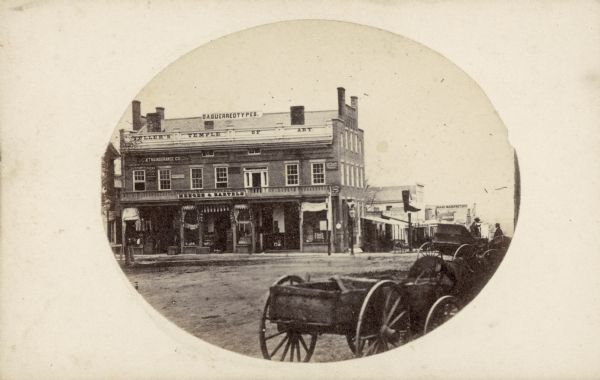Buildings on Pinckney Street, including the U.S. Hotel building and a carriage manufacturer. John S. Fuller's studio, "Fullers Temple of Art" was located in the U.S. Hotel building. Several people and horse-drawn buggies are in the foreground.