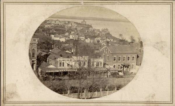 South Pinckney Street as photographed by Fuller from the Wisconsin State Capitol roof.  In the center are several wooden structures dating from Madison's earlier years. The State Bank, seen on the left, is typical of the more permanent stone buildings that were beginning to replace them.  The Williamson and Marquette neighborhoods are in the background and Governor Farwell's Octagon House is in the center on the shore of Lake Monona.