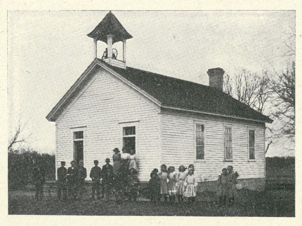 Exterior view of a schoolhouse in Cottage Grove with students posing in front of the building.