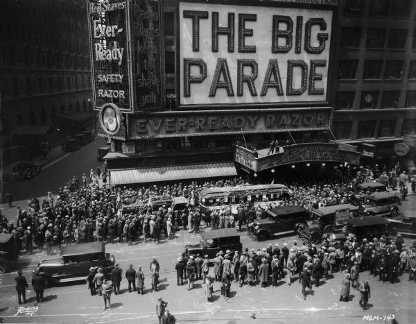 A crowd is gathered around MGM's "trackless train" outside the Astor Theater where "The Big Parade" is showing. Also visible is a gigantic advertisement for the Ever-Ready Safety Razor.