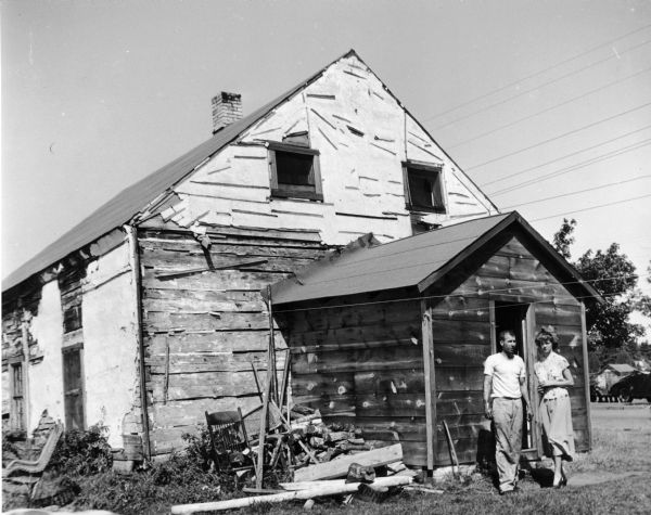 A young couple poses in front of a dilapidated house.