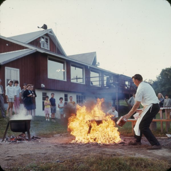 A man fueling a fire for a fish boil, as people look on.