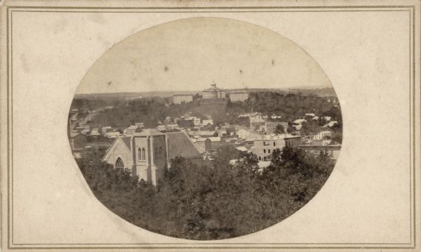 John S. Fuller made this photograph of the three University buildings on Bascom Hill (then known as College Hill) from the Capitol roof about 1860. Grace Episcopal Church, at the intersection of Carroll Street and West Washington Avenue, is prominent on the lower left. Today, it is one of only two buildings facing that Capitol Square that date from the 1850s. The foliage in the foreground documents the dense park that surrounded the Capitol.