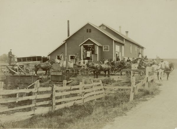 Building thought to be a cheese factory, with workers and horse-drawn delivery wagons in the front.