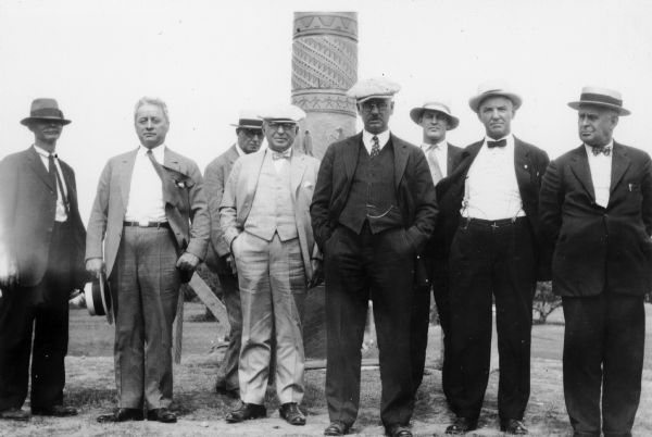 Eight men, including C.L. (Neal) Harrington, posing at a memorial pole together.