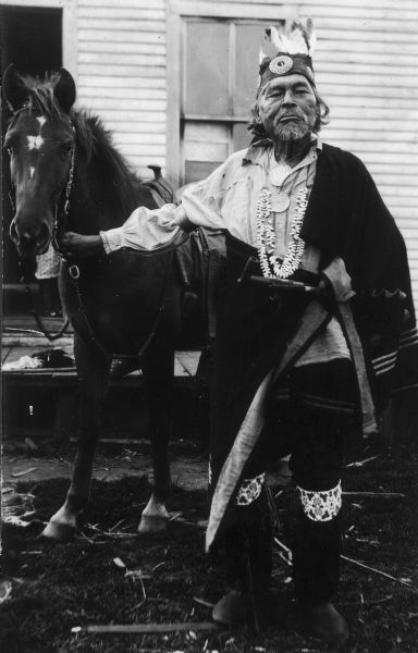 Candid portrait of Potawatomi Chief Simon Onanguisse Kahquados holding the bridle of a horse.