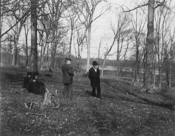 Outdoor view of two men standing and two women sitting in a grassy field. They are possibly members of the Park and Pleasure Drive Association, of which Charles Brown was an official.
