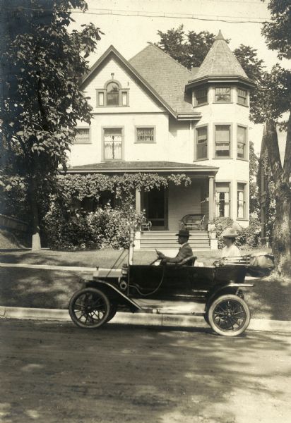 Albert G. Zimmerman driving with his wife in a Ford automobile past his house at 746 East Gorham Street.