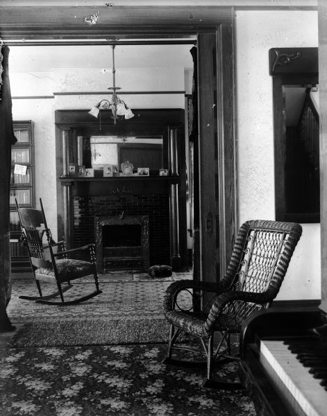 Interior view of the Albert G. Zimmerman house at 746 East Gorham Street. The view includes a fireplace, patterned carpeting and wicker chairs. In the foreground on the right is a piano.