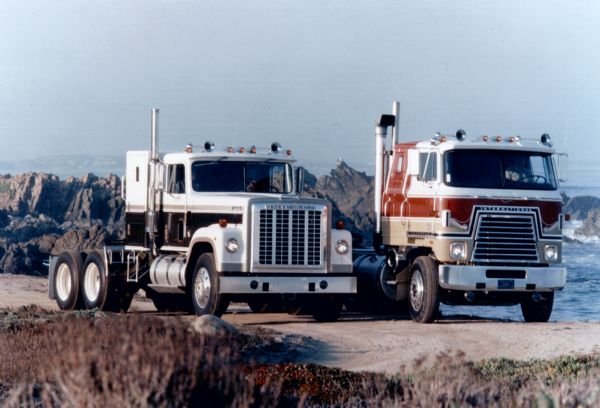 Color photograph of International Transtar Eagle Semi Tractors in the standard cab and cabover models parked beside a body of water.