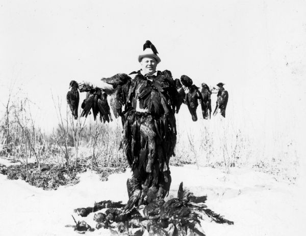 Oswald Neesvig, President of Madison (Wisconsin) Packing Company, draped in and standing among his quarry from a day of crow hunting.