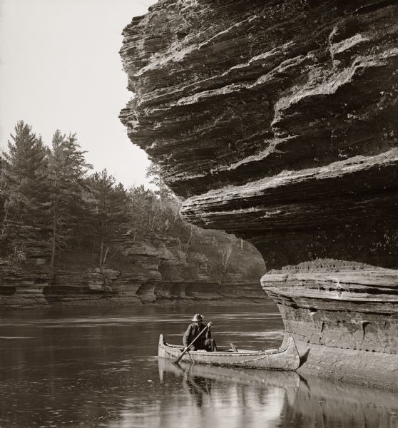 Berry's landing; man in a canoe under overhanging cliff.