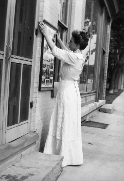 Evaline Bennett, wife of Henry Hamilton Bennett, in a white dress  outside the studio hanging framed images.