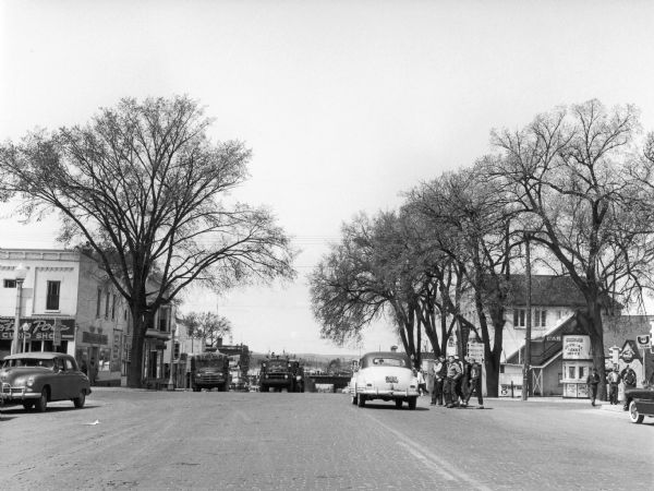 A view down tree-lined Broadway showing vehicles and a group of boys crossing the street.