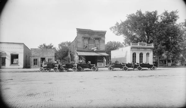 Street scene featuring the Ford Garage and the Bowman Bank. Several cars are parked in front of the buildings.