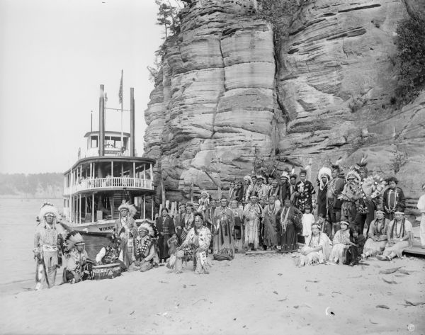 Ceremonial performers in traditional Indian costume pose near a steamboat.