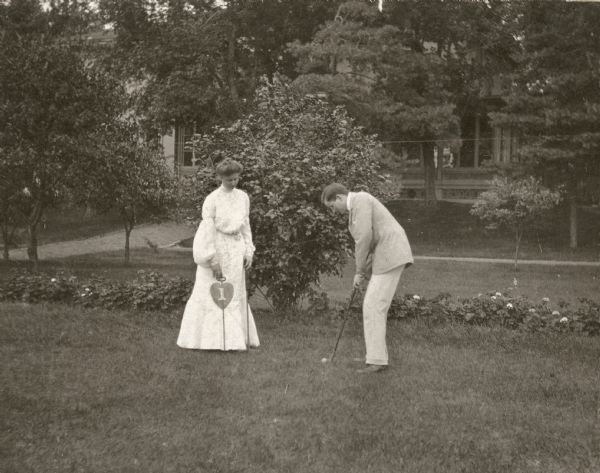 A man and woman golf on the west lawn of Villa Louis. They are probably members of the Dousman family.