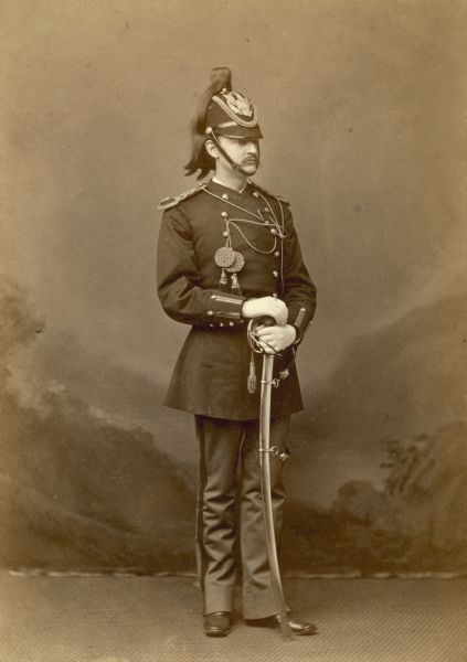 Full-length studio portrait of Lee Alexander standing in military uniform, including an elaborate helmet and sword.