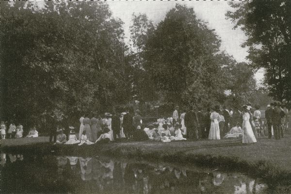 A group of formally dressed people gather at Tenney Park to hear a band concert.