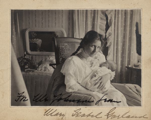Zulime Taft Garland, wife of Hamlin Garland, holds their infant daughter Mary Isabel while sitting in a rocking chair.