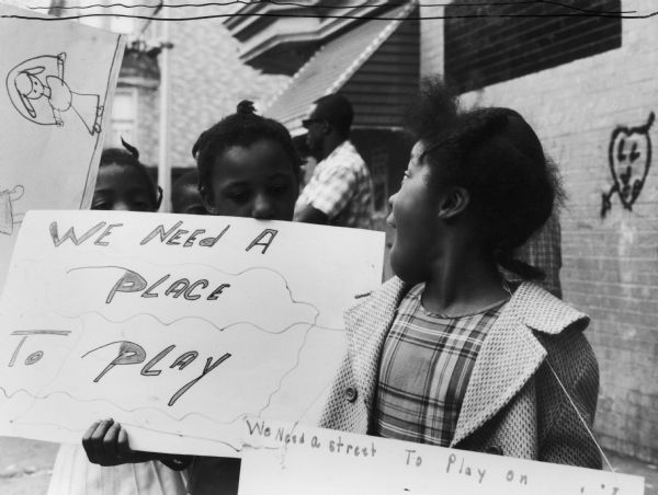 Children hold signs that read "We Need A Place To Play" and "We Need a Street to Play On," which is related to the Newark Community Union Project.