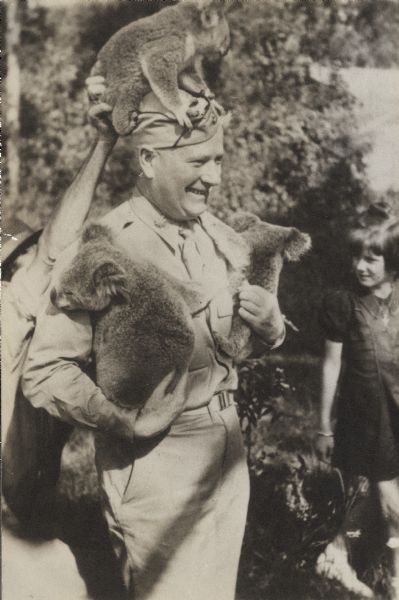 Former Wisconsin Governor Philip La Follette wearing his World War II uniform and holding two koala bears with a third koala on his head.