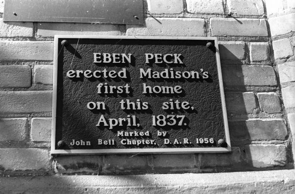 Bronze historical marker affixed to the back of the Capitol Hotel at 208 King Street on which are the words, "Eben Peck erected Madison's first home on this site, April, 1837.".