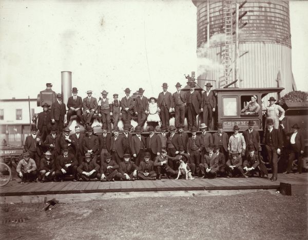Special train from Spooner, Wisconsin, to Union Meeting at St. Paul, Minnesota. Group portrait of men posing on and around the locomotive. A young girl is standing in the center of the top row. A dog is sitting on the platform in front of the group.