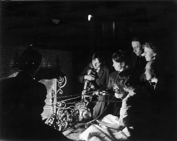 Seven people gather around the fireplace at the home of Professor Jacobson, toasting marshamallows (probably).