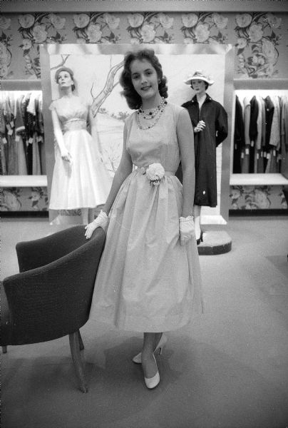 Colleen O'Brien, sophomore at East High School, modeling a light blue cotton Dacron dress, with her hand resting on the back of a chair, for a Vogue pattern fashion show at Manchester's women's clothing store.
