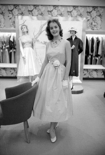 Colleen O'Brien, sophomore at East High School, modeling a light blue cotton Dacron dress, with her hand resting on the back of a chair, for a Vogue pattern fashion show at Harry S. Manchester women's clothing store.