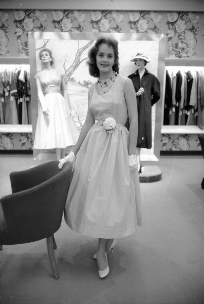 Colleen O'Brien, sophomore at East High School, modeling a light blue cotton Dacron dress, with her hand resting on the back of a chair, for a Vogue pattern fashion show at Manchester's.