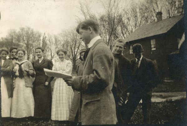 A young man reads to a group standing outside Hillside Home School.