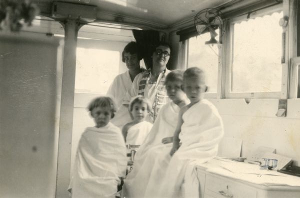 Four siblings await their physical examination. Three of the children are triplets. In the background are the public health nurse and examining physician.