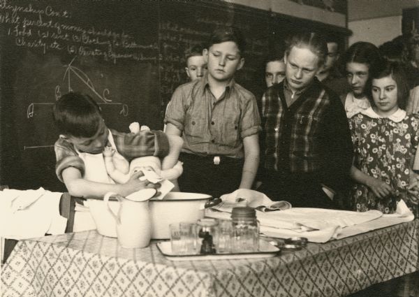 A boy is bathing a doll in Infant Hygiene Class while other classmates watch.