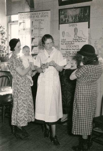 A nurse instructs two mothers about baby shoes.