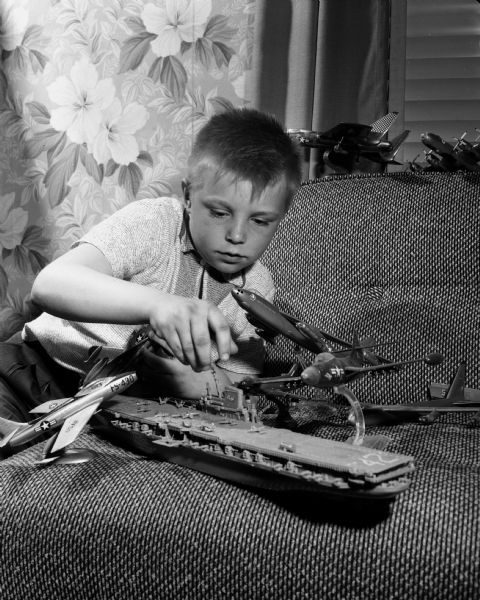 Young boy with toy airplanes and an aircraft carrier.
