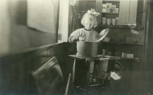 A young girl is preparing lunch in a pot on a small stove.