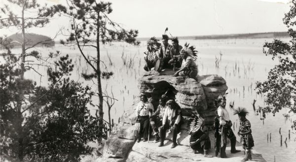 A group of Indians, probably Ho-Chunk, in traditional costume, posing on and around Demon's Anvil.