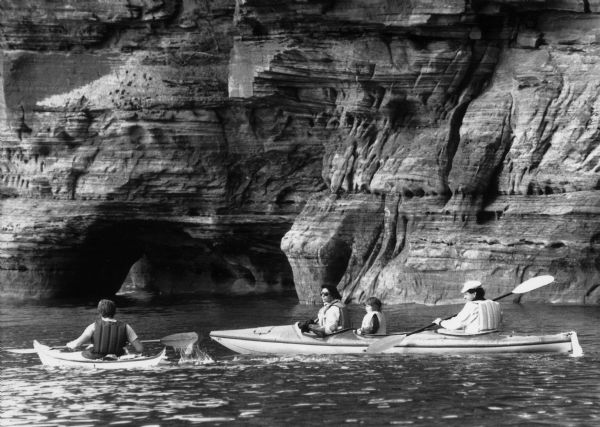 A family kayaks in front of rock walls at the Apostle Islands.