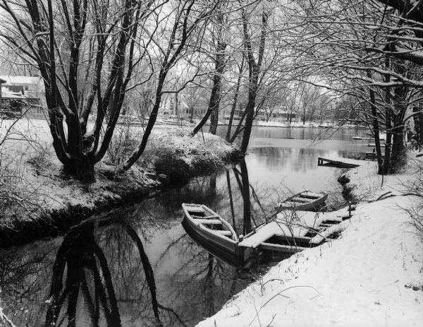 Two rowboats docked in a river surrounded by trees, following a recent snowfall.