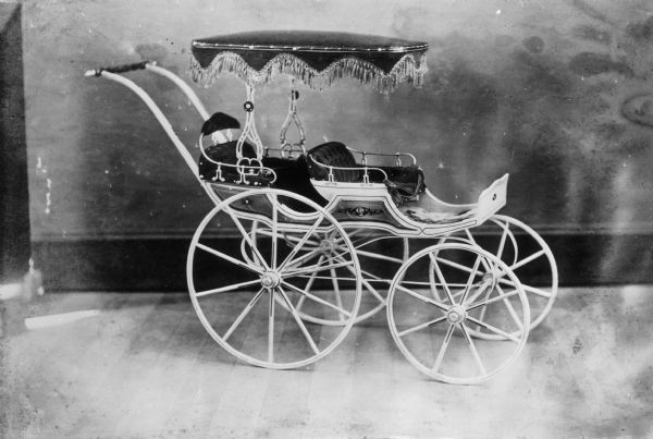 Two seat children's carriage with small tasselled canopy, produced at children's carriage factory.