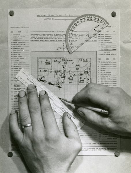 Person's hands, one with with wedding ring on left hand, using a ruler, pencil, and protractor to draw a land cover map for Wisconsin Land Economic Inventory.